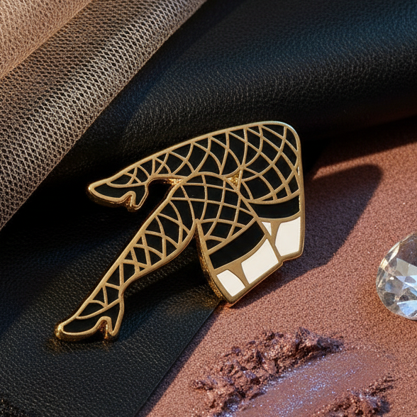 Fishnet Stockings Enamel Pin features gold-tone crossed legs in fishnets and heels, surrounded by luxe beige tulle, black faux-leather, a rhinestone, and shimmering lavender-pink powder, celebrating bold, proud, queer self-expression.