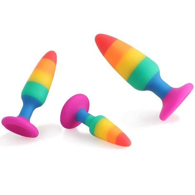 Three rainbow-striped silicone butt plugs with bright pink flared bases on a white background
