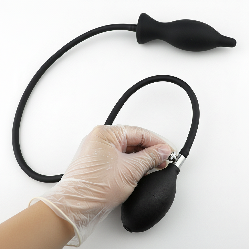 Gloved hand holds a black bulb pump connected by tubing to an inflatable dildo
