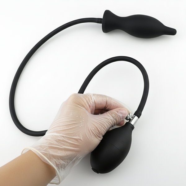 Gloved hand holds a black bulb pump connected by tubing to an inflatable dildo