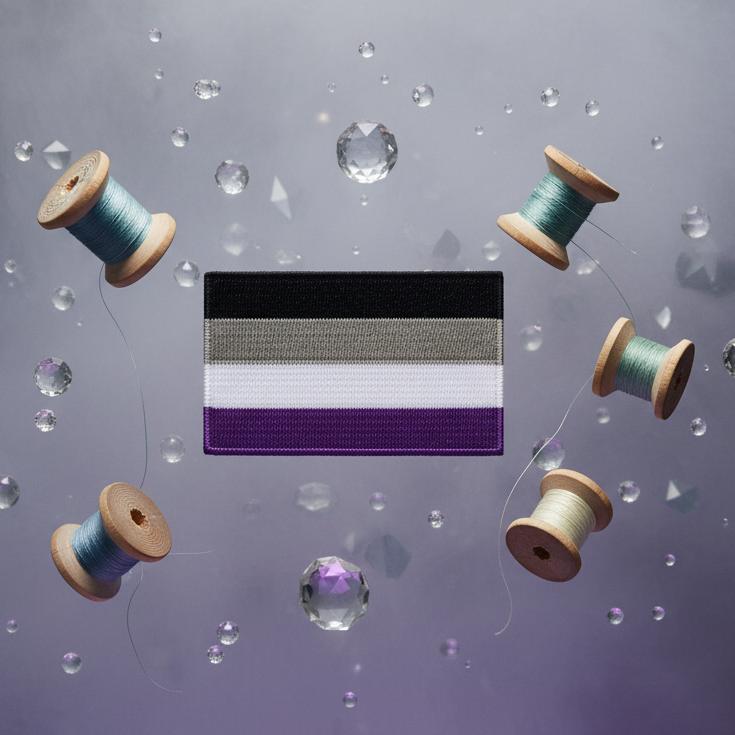 A rectangular asexual pride flag patch with black, gray, white, and purple stripes, surrounded by thread spools