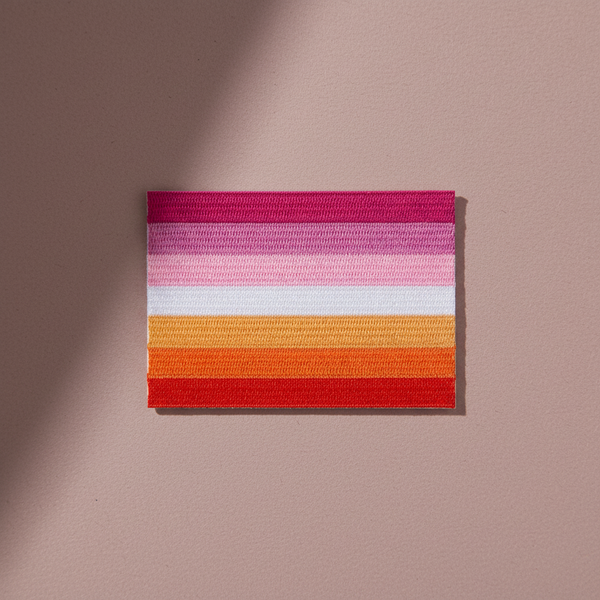 Lesbian Flag iron-on embroidered patch with dark pink, pink, white, orange, and red stripes on mauve background and shadow.