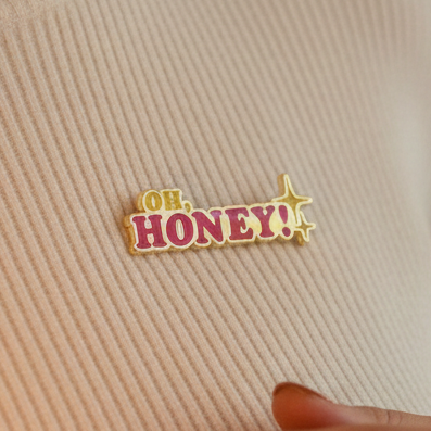 Oh Honey! enamel pin with red and yellow lettering on a ribbed fabric background