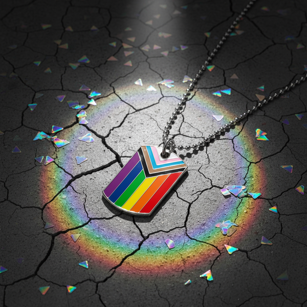 Progress Pride flag tag necklace on a ball chain, photographed on cracked dark ground
