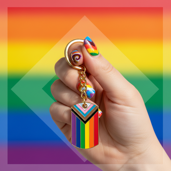 Progress Pride rainbow enamel keychain held against a rainbow flag background