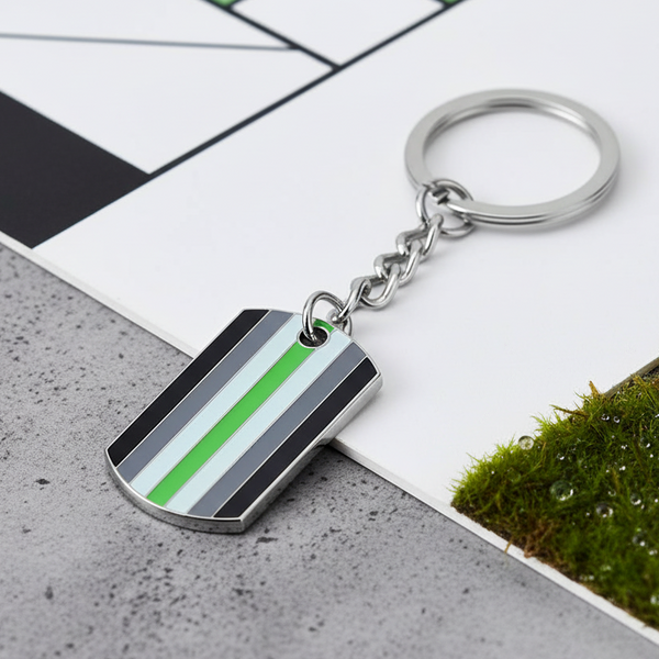 Agender pride keychain with striped dog-tag pendant and silver ring on a tiled surface