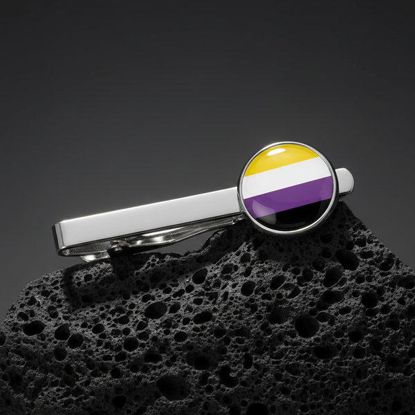 Non-Binary Pride tie clip with a round yellow, white, purple, and black flag emblem on silver, shown on black volcanic rock.
