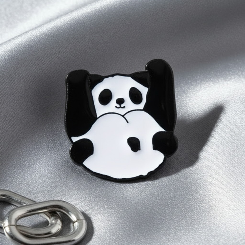 Black-and-white panda enamel pin sitting on shiny silver fabric