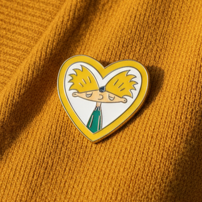 Close-up of a heart-shaped Hey Arnold enamel pin on mustard ribbed fabric