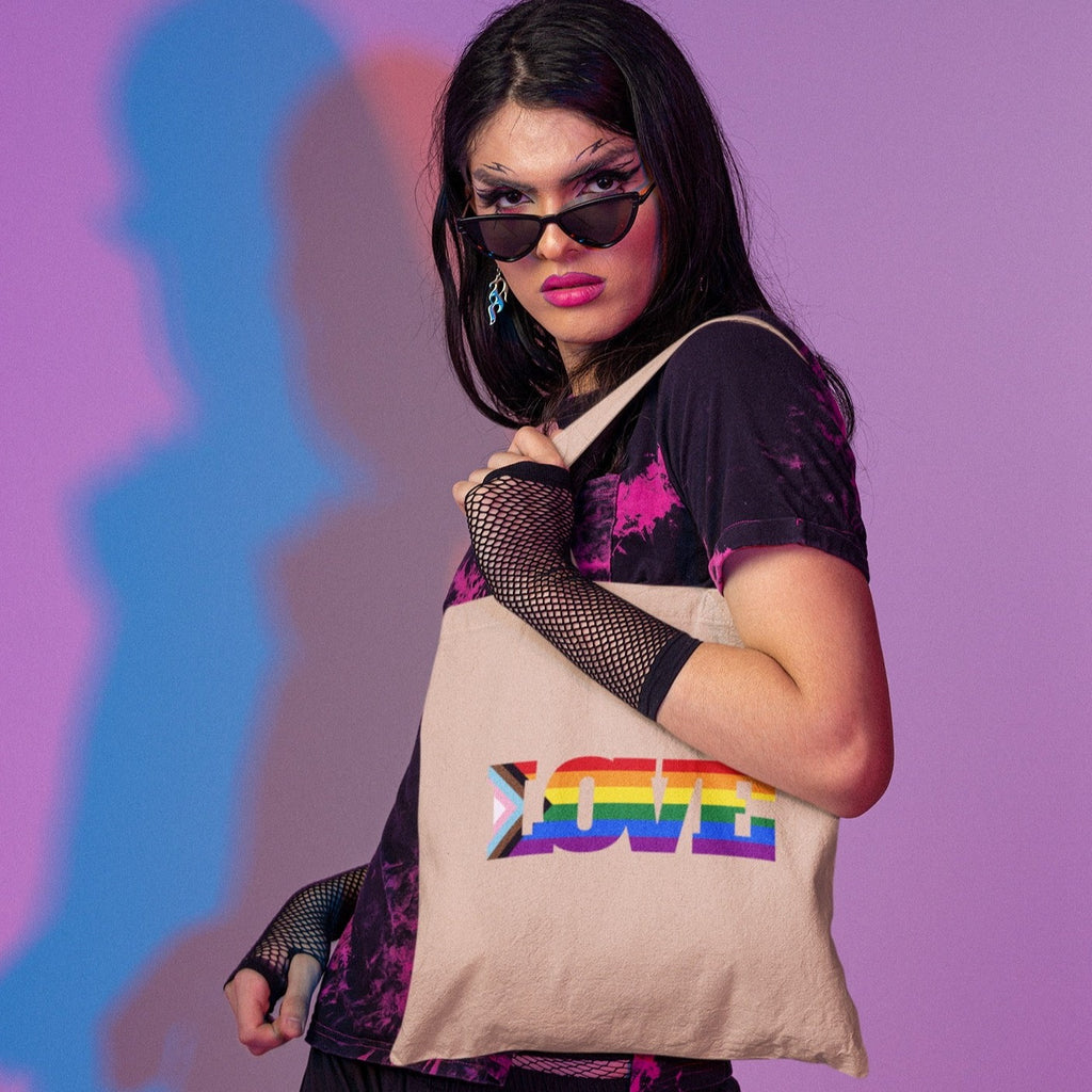 Model holding a beige tote with colorful Progress Pride flag lettering