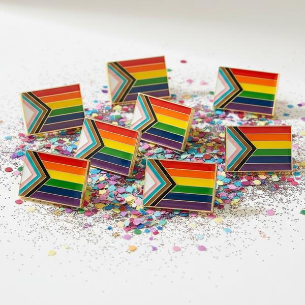 Progress Pride flag enamel pins arranged on colorful confetti