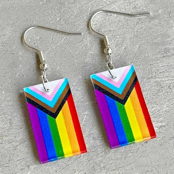 Pair of rectangular acrylic Progress Pride flag earrings shown flat on a gray textured surface