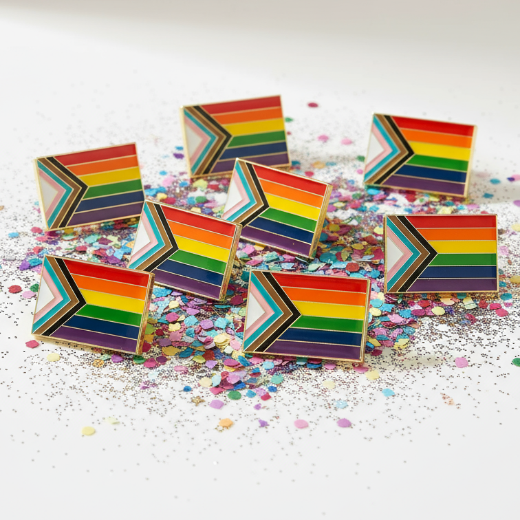 Progress Pride flag enamel pins arranged on colorful confetti