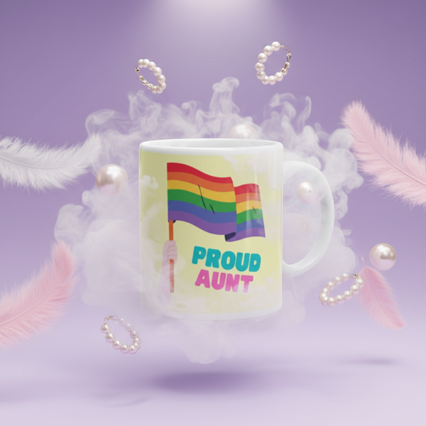 White mug reading “PROUD AUNT” beneath a rainbow flag, staged amid feathers and pearls