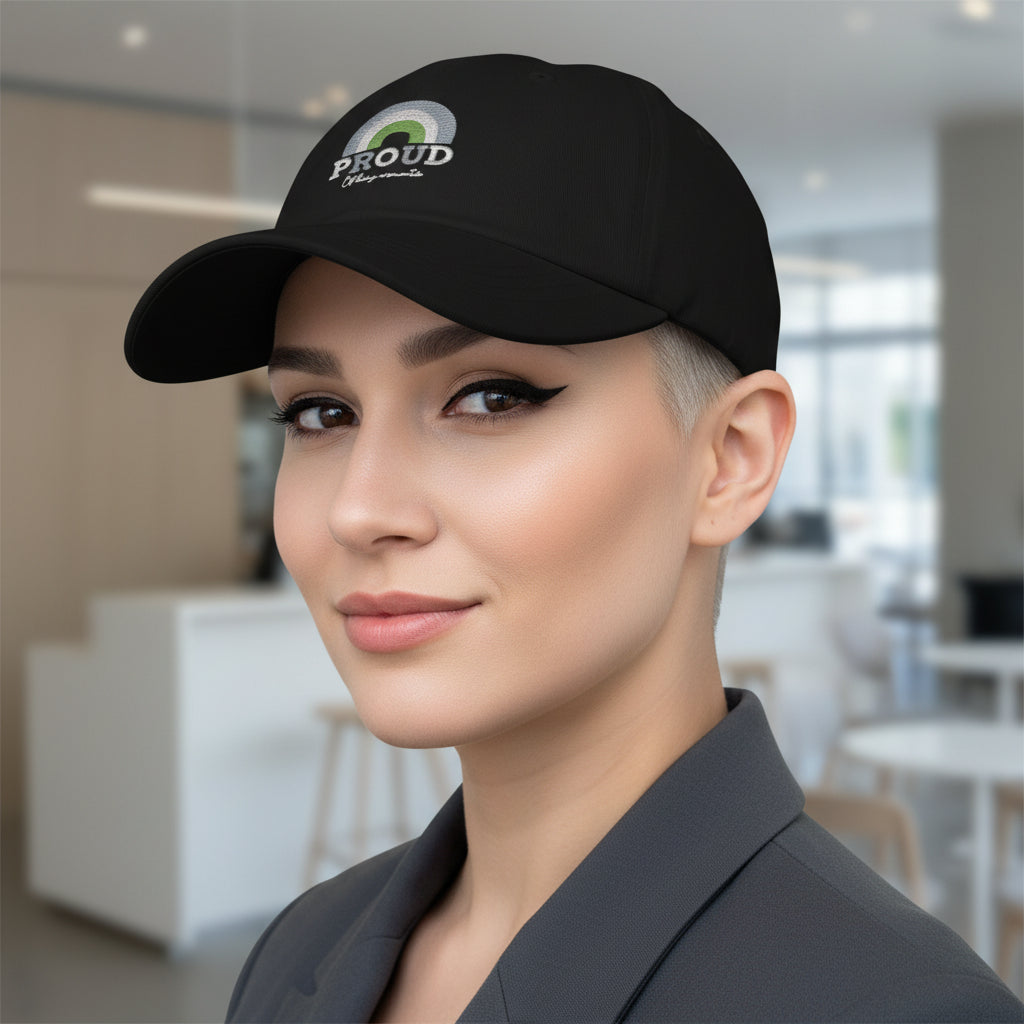 Proud Of Being Aromantic Cap" with rainbow detail, worn by a short-haired person in a gray blazer at a bright, modern cafe.