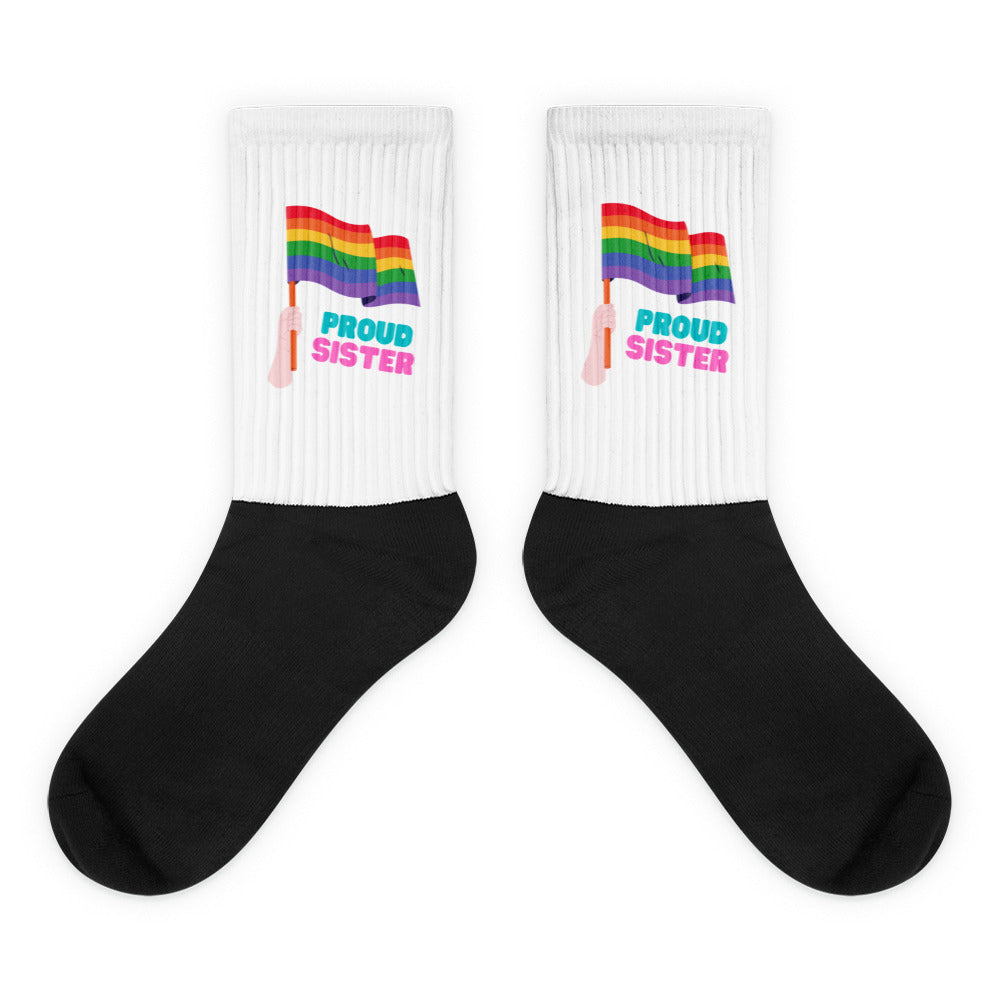 Pair of crew socks with black feet, white ribbed cuffs, rainbow flags, and “PROUD SISTER” text