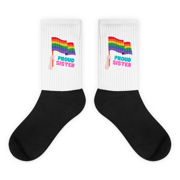 Pair of crew socks with black feet, white ribbed cuffs, rainbow flags, and “PROUD SISTER” text