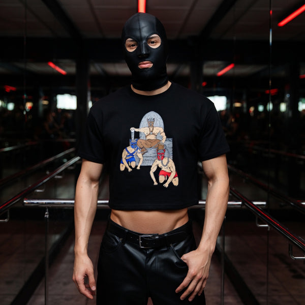 Front-facing person in a black crop top with a throne-and-pups graphic, wearing a black pup mask