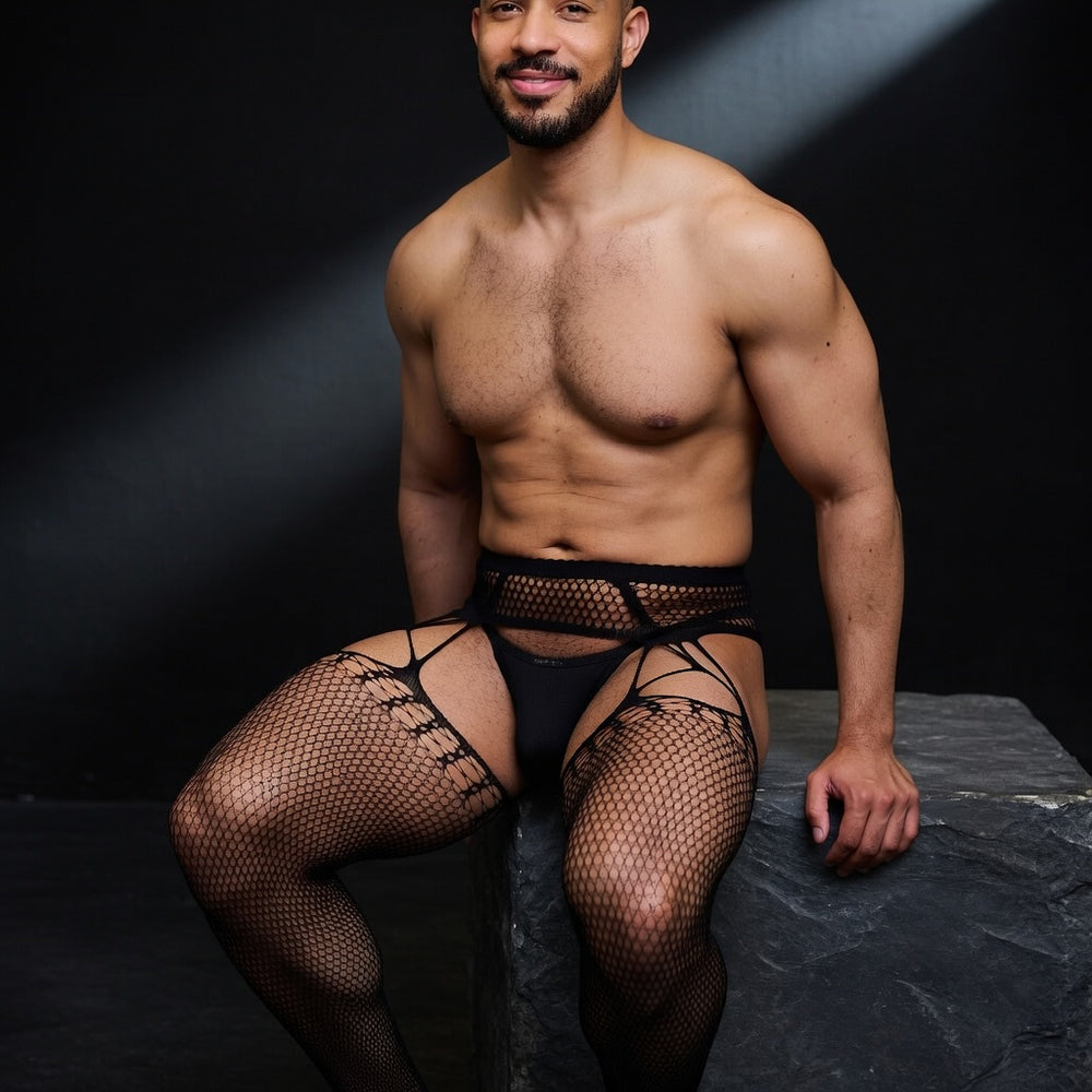 Adult male model wearing men's patterned pantyhose in the Entice design, seated on dark stone, with opaque black underwear.