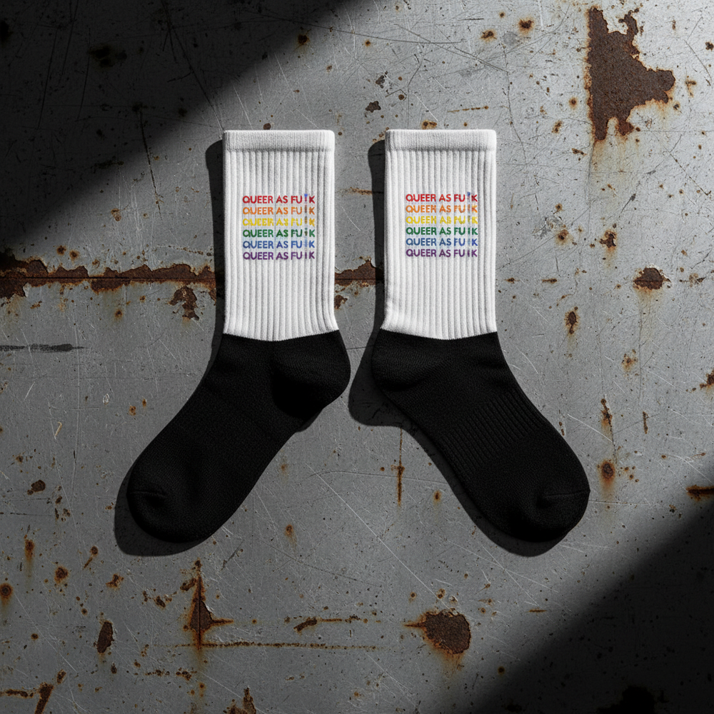 Crew-length black-and-white socks with "QUEER AS F*#K" in rainbow colors, stacked five times on white; black toes and heels.