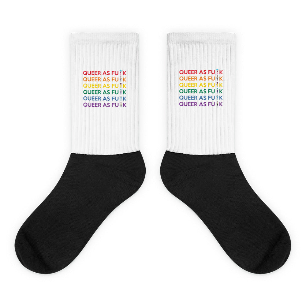 Pair of black-and-white crew socks with rainbow “QUEER AS FU*K” text on the cuffs