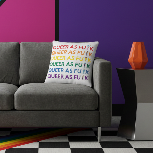 Gray sofa with a “Queer As Fu#k” Premium Pillow in rainbow colors, against a purple-magenta wall