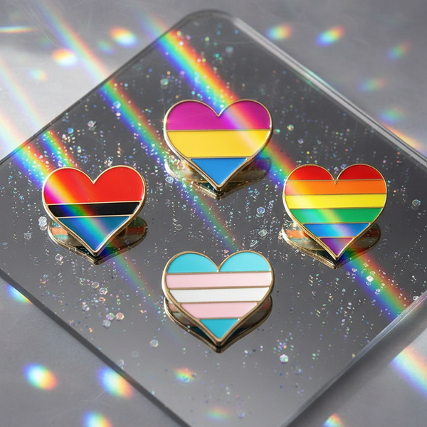 Four heart-shaped enamel pins with pride-style rainbow stripes on a glittery mirrored surface
