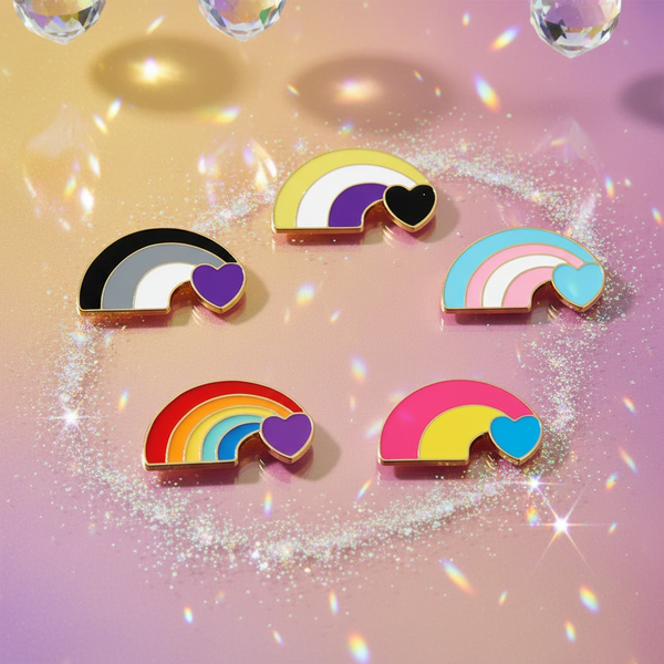 Five rainbow-and-heart enamel pins arranged on a glittery pink and yellow background