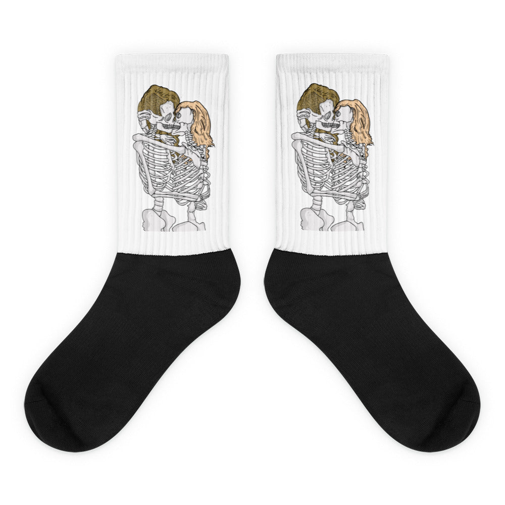 Pair of black crew socks with white cuffs showing two skeletons kissing