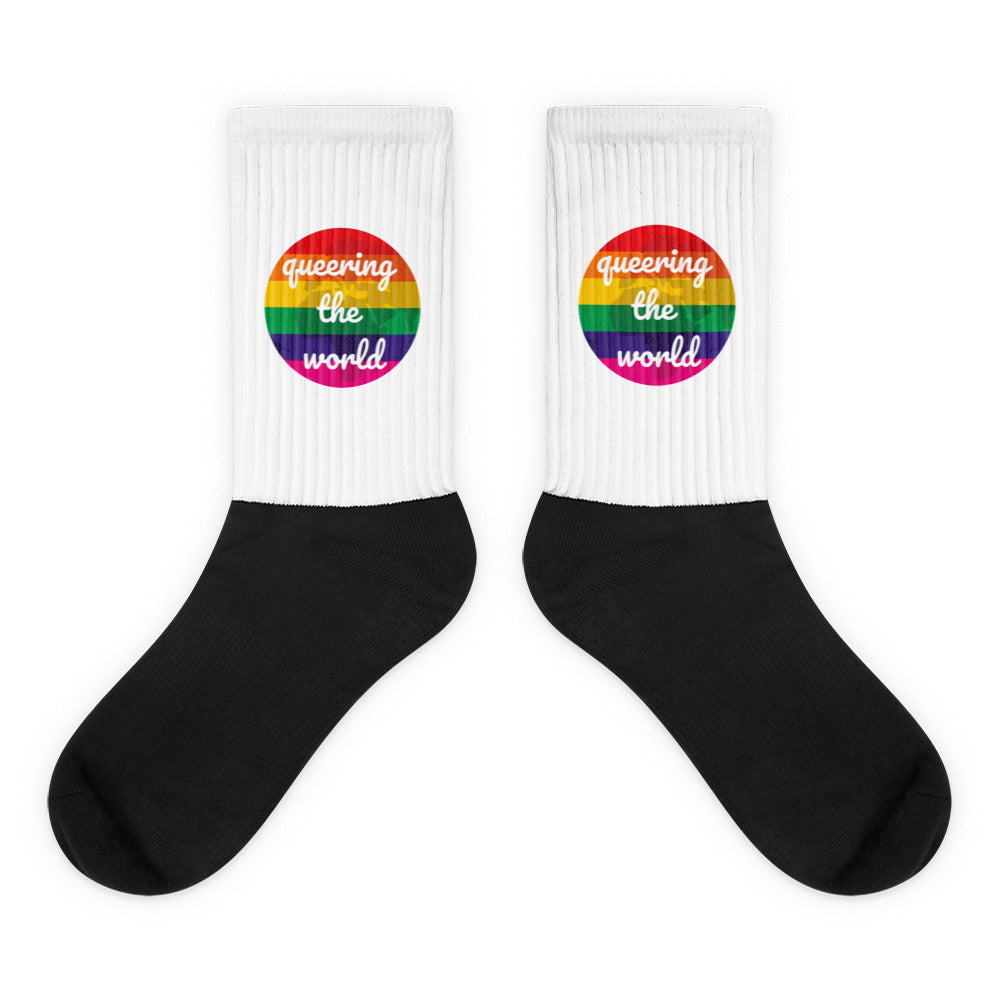 Pair of black-and-white crew socks with rainbow badges reading “queering the world”
