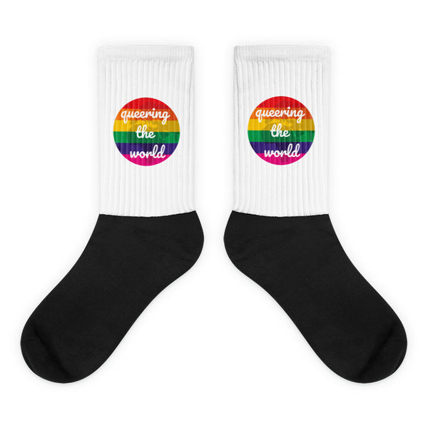 Pair of black-and-white crew socks with rainbow badges reading “queering the world”