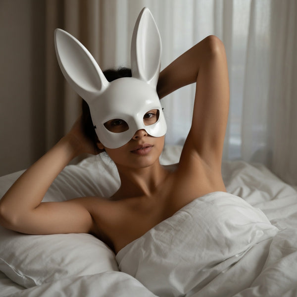 Person reclining in bed wearing a glossy white rabbit mask with tall ears and eye cutouts