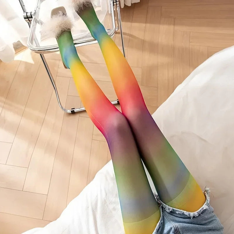 Rainbow-gradient tights on crossed legs, shown from above beside a bed