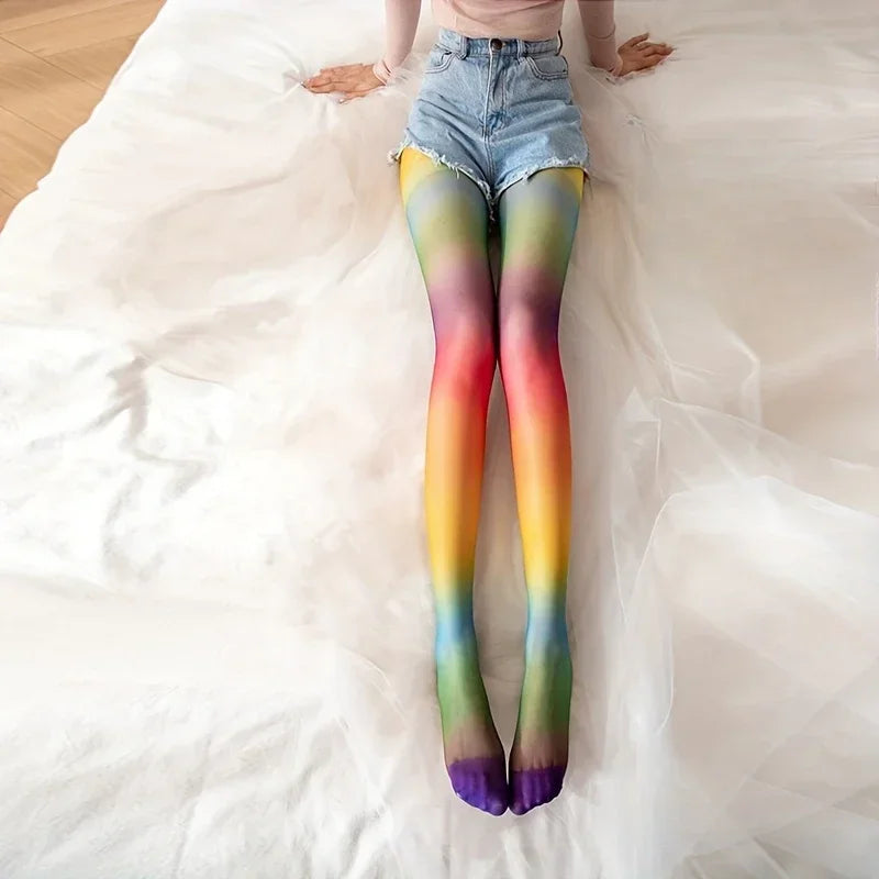 Model lying on a white bed wearing rainbow gradient tights with blue denim shorts