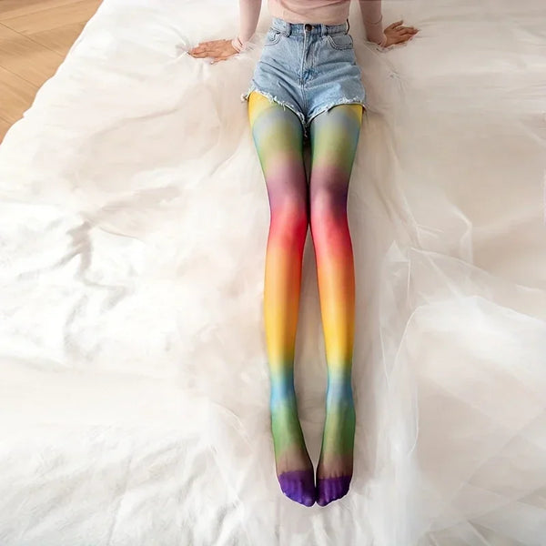 Model lying on a white bed wearing rainbow gradient tights with blue denim shorts
