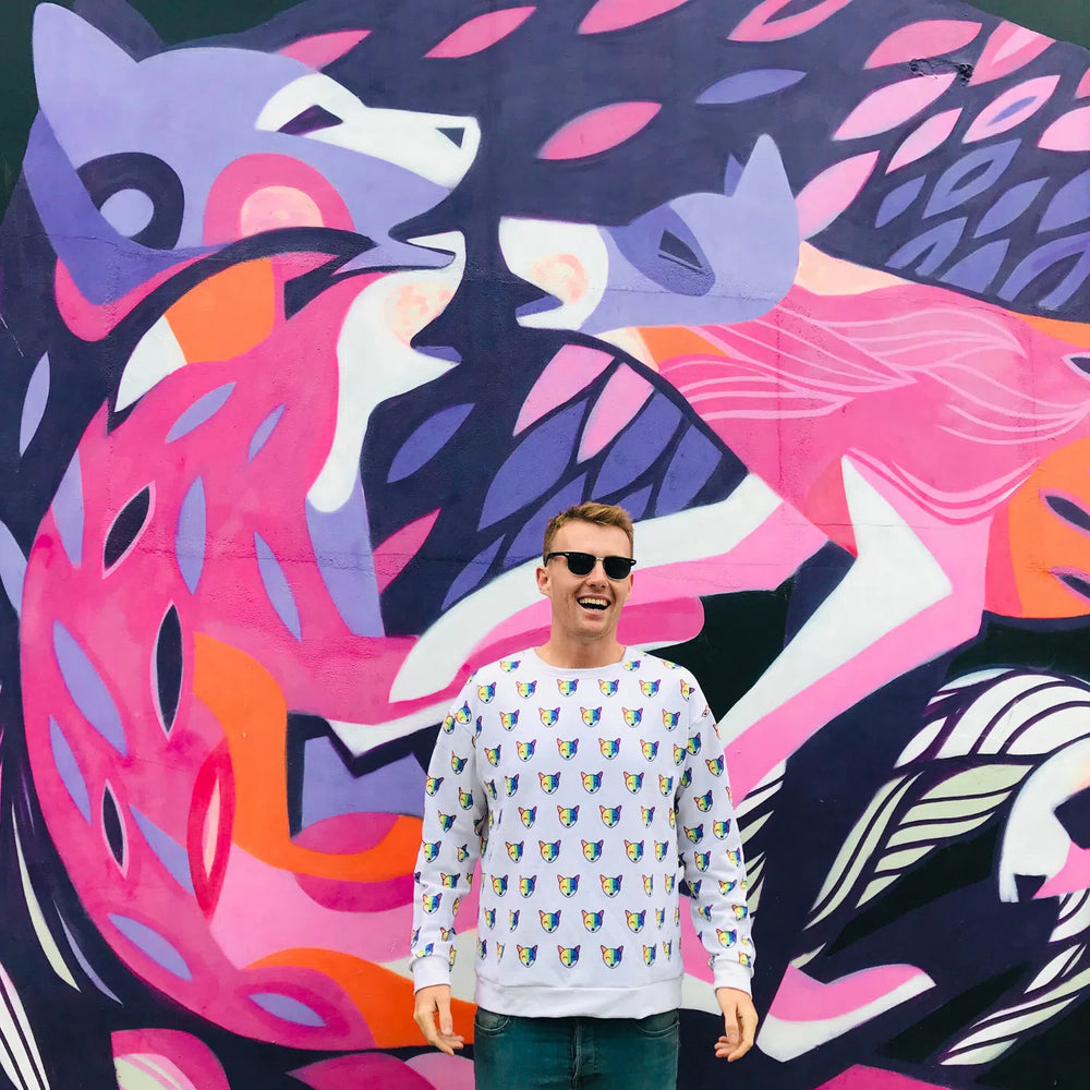 Person wearing a white sweatshirt covered in rainbow fox faces before a colorful mural