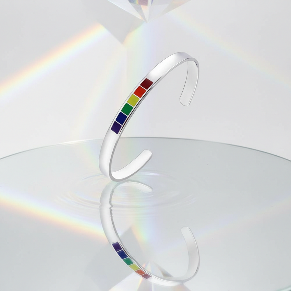 Silver open-cuff bangle with six rainbow-colored rectangular insets, shown upright on a reflective surface