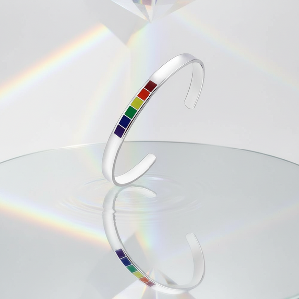 Silver open-cuff bangle with six rainbow-colored rectangular insets, shown upright on a reflective surface