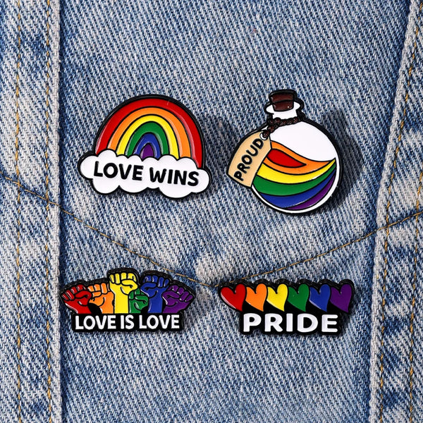 Four rainbow Pride enamel pins on denim, including “LOVE WINS,” “LOVE IS LOVE,” and “PRIDE” designs