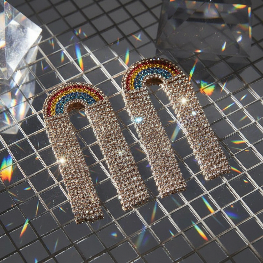 Rainbow rhinestone arch earrings on a reflective grid surface