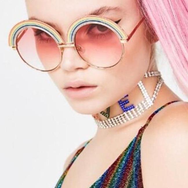 Model wearing round rainbow-striped sunglasses with pink gradient lenses