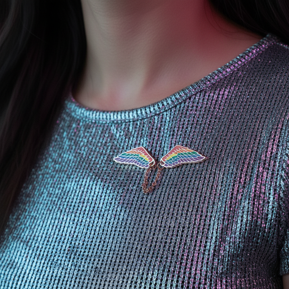 Close-up of rainbow wing enamel pins worn on a shimmering dark shirt