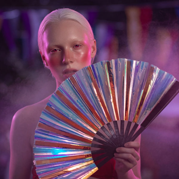 Person holds an open iridescent folding fan in pink and purple light