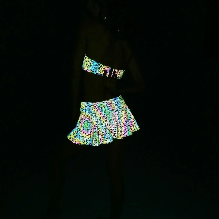 Model wearing a reflective rainbow scribble-print pleated skirt in near darkness