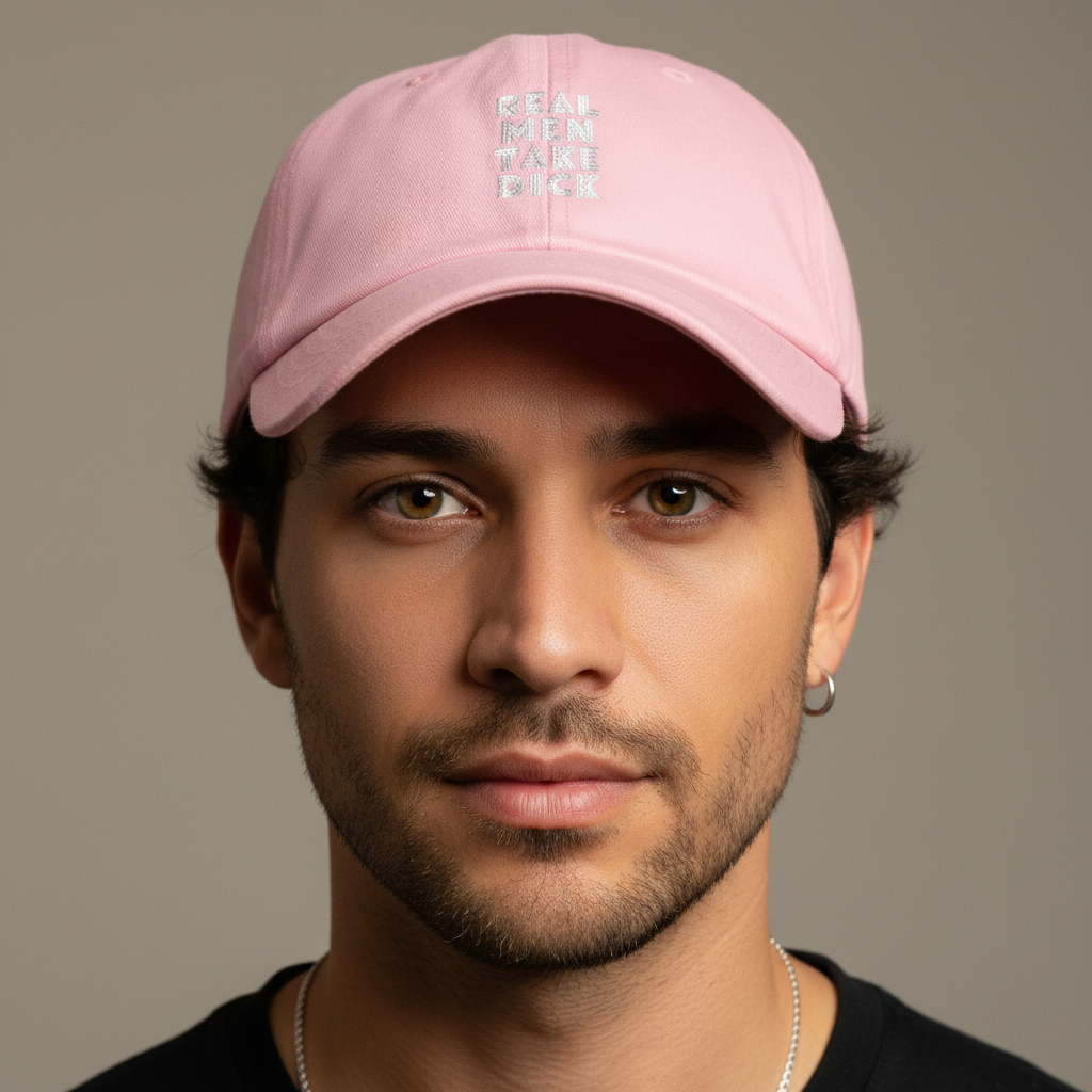 Pink "Real Men Take Dick" cap on a light-skinned young man with short dark hair, hazel eyes, and a small left hoop earring.