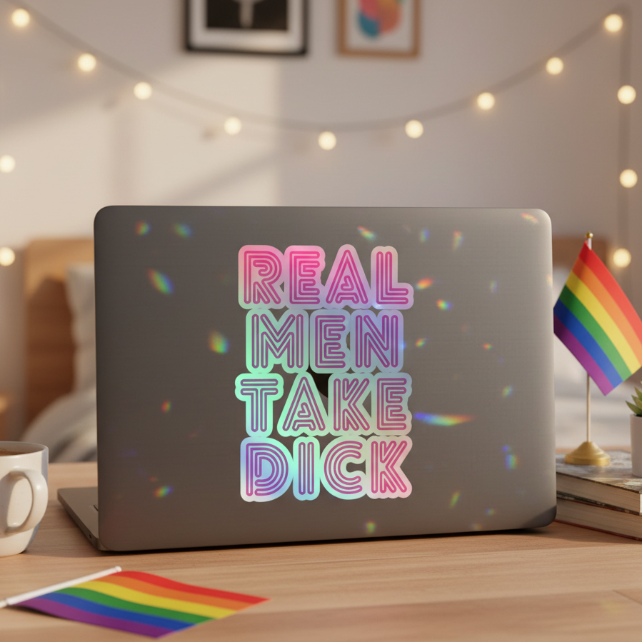 Laptop on a wooden desk with a holographic “Real Men Take Dick” sticker, queer decals, pride flags, mug