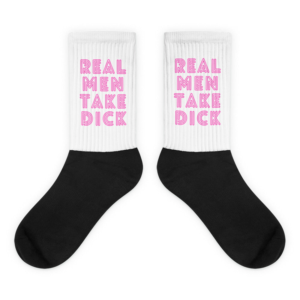 Pair of black-and-white socks with pink “REAL MEN TAKE DICK” lettering