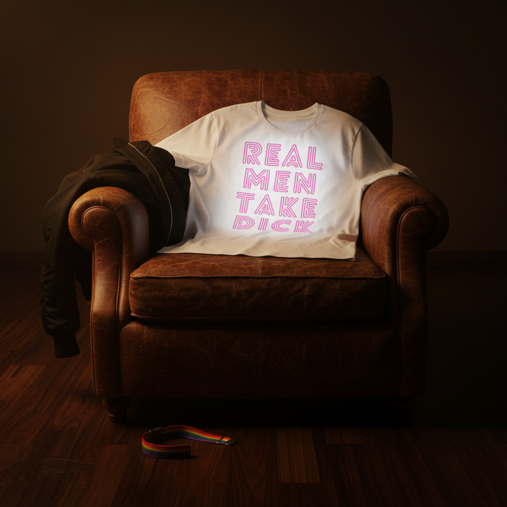 White T-shirt reading “REAL MEN TAKE DICK” draped over a leather armchair