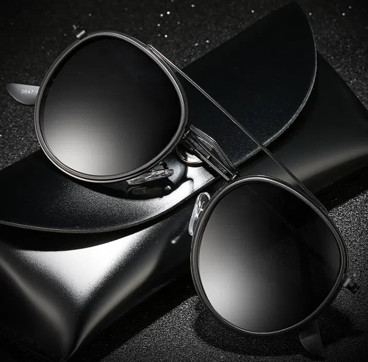 Round black sunglasses with dark lenses resting on a black case and hat