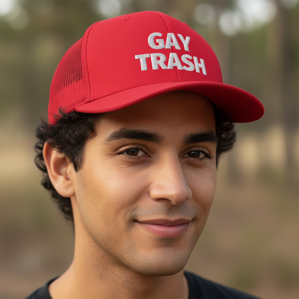 Gay Trash Trucker Cap in bright red mesh, “GAY TRASH” bold white letters, worn by a queer person with short curly hair.